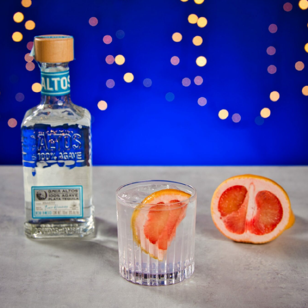 Paloma drink på et bord med en flaske Altos Plata Tequila og en grapefrugt.