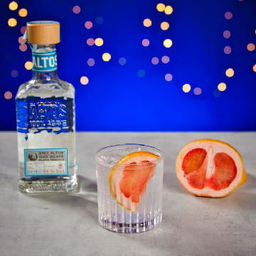 Paloma drink på et bord med en flaske Altos Plata Tequila og en grapefrugt.