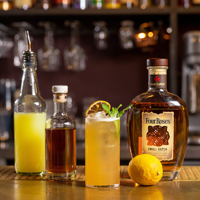 Kentucky Cooler cocktail på et bord med en flaske Four Roses Small Batch og citron.