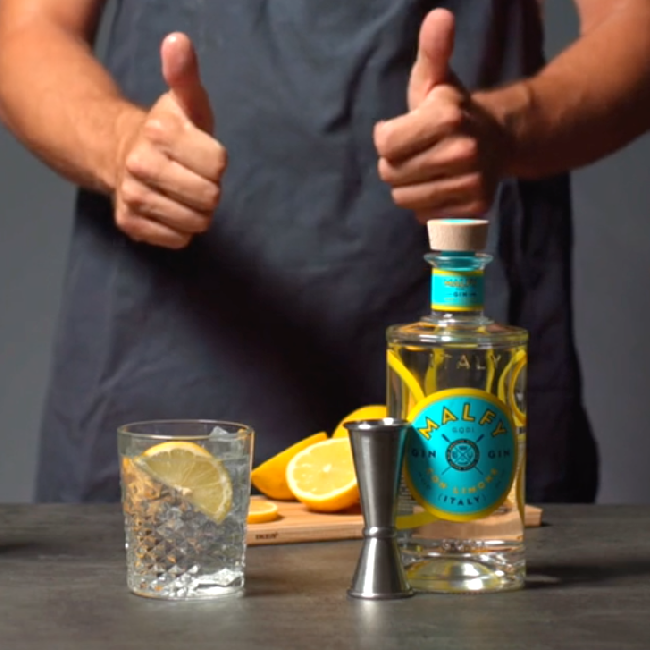 Malfy Limone Twist drink på et bord med en flask Malfy con Limone og citroner.
