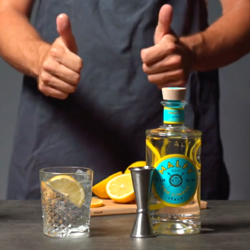 Malfy Limone Twist drink på et bord med en flask Malfy con Limone og citroner.
