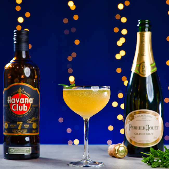 Old Cuban cocktail på et bord med en flaske Havana Club 7 og Perrier Jouët Grand Brut