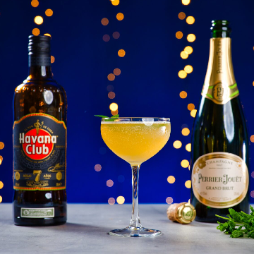 Old Cuban cocktail på et bord med en flaske Havana Club 7 og Perrier Jouët Grand Brut