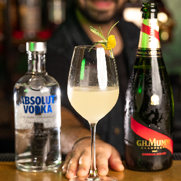 Queen Bee drink i et hvidvinsglas med en flaske Absolut Vodka og G.H. MUMM Cordon Rouge Brut Champagne