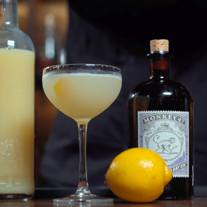 Bee's knees cocktail på et bord med en flaske Monkey 47 gin og en citron