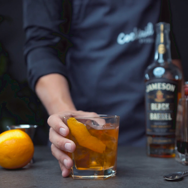 Old fashioned drink på et bord med en flaske Jameson Whiskey Black Barrel og en appelsin.