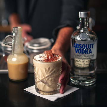 En Whiteish Russian cocktail på et bord med en flaske Absolut Vodka.