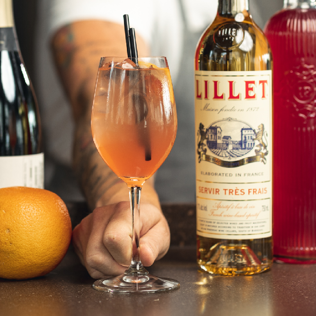 Nærvær Rabarber Spritz drink serveret i et vinglas med en flaske Lillet blanc og champagne.