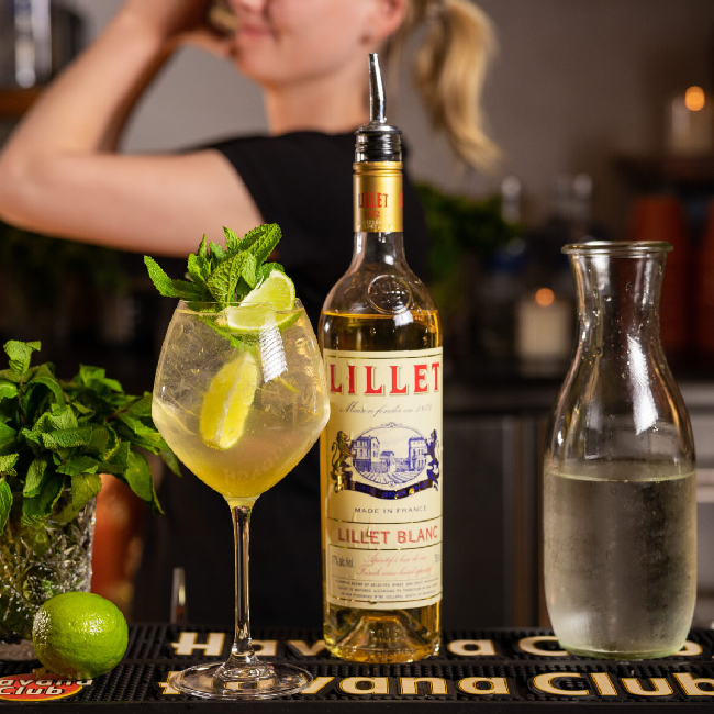 Lillet Hugo Spritz drink i et vinglas med en flaske Lillet Blanc og lime.