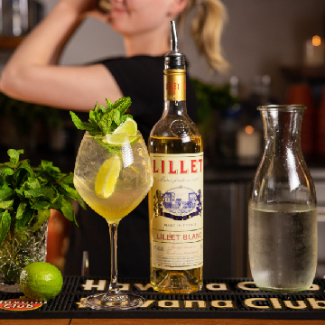 Lillet Hugo Spritz drink i et vinglas med en flaske Lillet Blanc og lime.