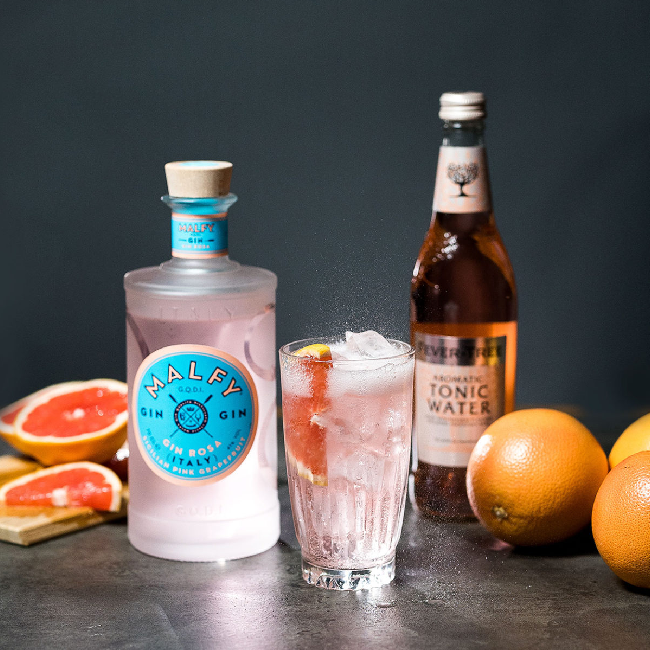 Malfy Rosa Twist drink på et bord med en flaske Malfy Gin Rosa og grapefrugter.