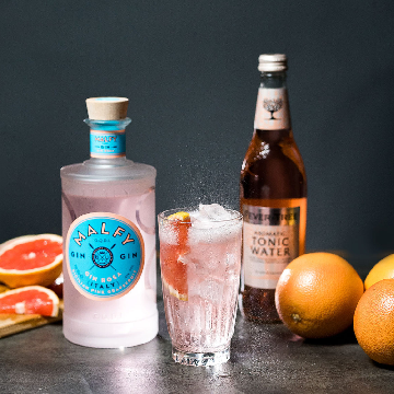 Malfy Rosa Twist drink på et bord med en flaske Malfy Gin Rosa og grapefrugter.