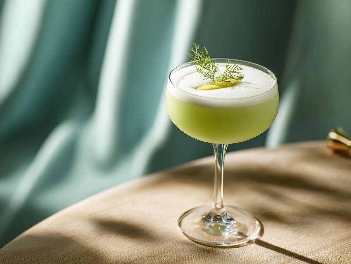 A bright green colored drink in a coupeglass, served on a wooden table. Created by AI. Edited by Pernod Ricard Sweden