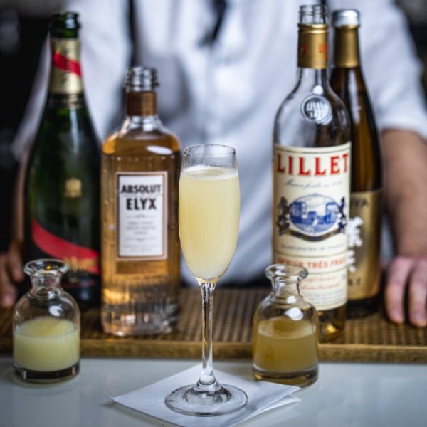 Jin-Gin cocktail på et bord med en flaske Absolut Elyx Vodka, Lillet Blanc og en G.H. Mumm Cordon Rouge Brut Champagne.
