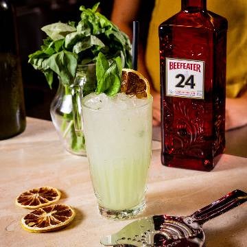 En gin basil smash cocktail på et bord med en flaske Beefeater Gin 24.