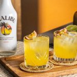 2 Sunset Passion cocktails på et bord md en flaske Malibu rom.