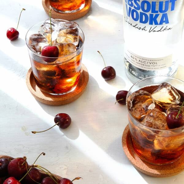 Black Russian cocktail på et bord med kirsebær og en flaske Absolut Vodka