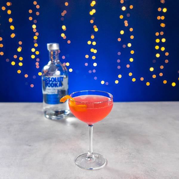 Cosmopolitan cocktail på et bord med en flaske Absolut Vodka