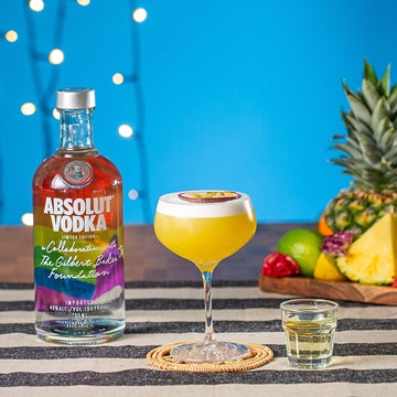 En Pornstar Martini cocktail og et shot 'bobler' på et bord. En flaske Absolut Vodka og et frugtfad.