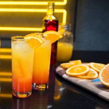 To Tequila Sunrise cocktails på et bord appelsiner og en flaske grenadine