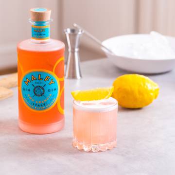 En Arancia Sour cocktail på et bord med en flaske Malfy Gin con Arancia.