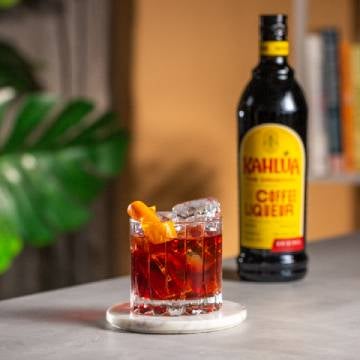 Coffee Negroni drink på et bord med en flaske Kahlúa.