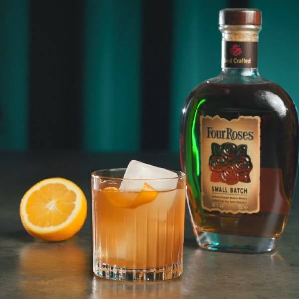 Old Fashioned cocktail på et bord med en flaske Four Roses og appelsin