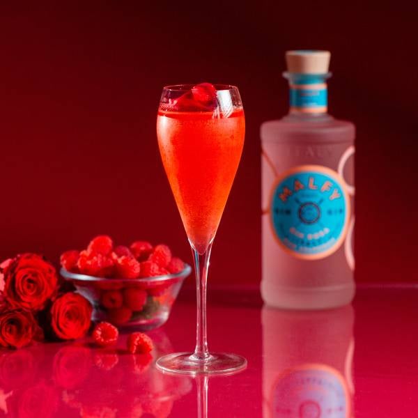 Rosa Cheeks cocktail på lyserødt bord med en flaske Malfy Gin Rosa og hindbær i en skål,