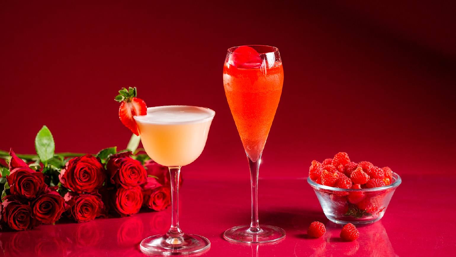 2 valentines cocktails på et bord. En buket roser og en skål med hindbær.