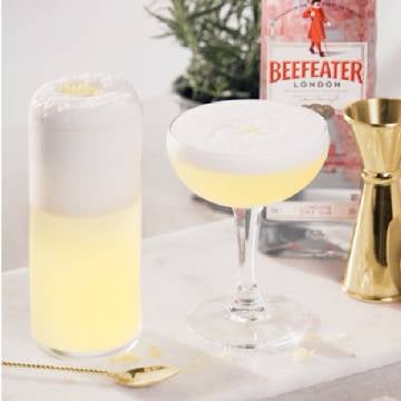 Gin Fizz cocktails på et bord med en jigger, barske og en flaske Beefeater Dry Gin.