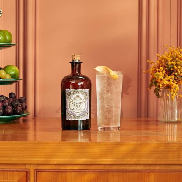 Gin & Tonic drink på et bord med en flaske Monkey 47 Dry Gin, blomster og frugter på et fad.