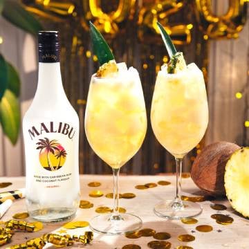 Malibu Sparkling Pina Colada cocktails på et bord med en flaske Malibu og ananas.