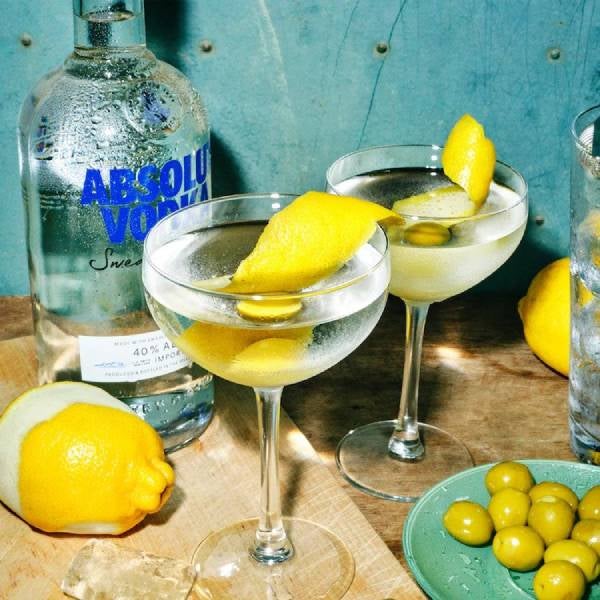 2 Vodka Martini drinks på et bord med en flaske Absolut Vodka, citroner og grønne oliven.