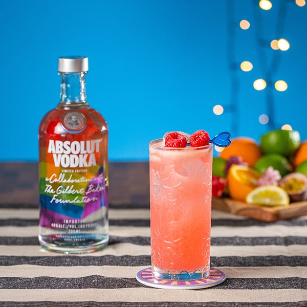 En Raspberry Fizz cocktail, en flaske Absolut Vodka og en kurv med frugt.