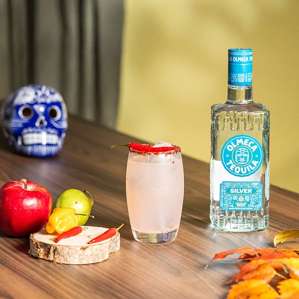 Spicy Paloma drink på et bord ved siden af en flaske Olmeca Tequila