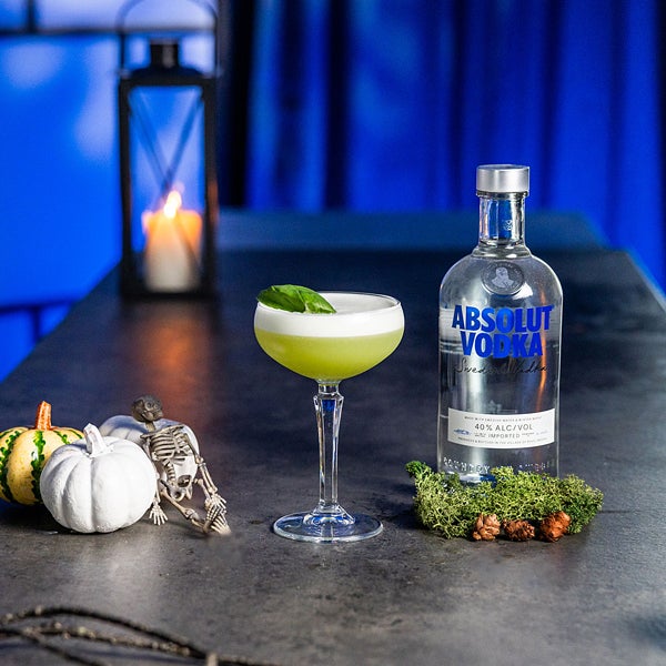 Kiwi Sour cocktail på et bord med en flaske Absolut Vodka