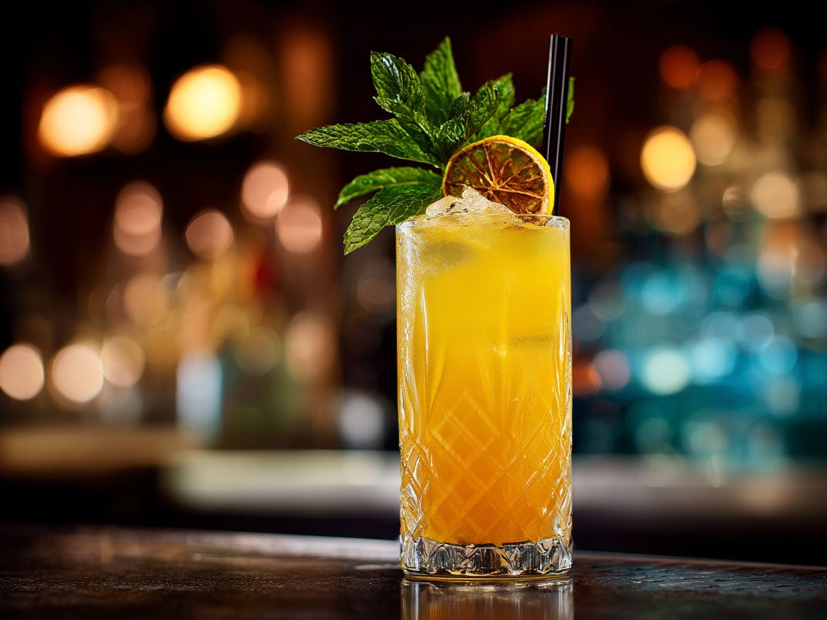 A orange colored cocktail placed on top of a bar. Garnished with lime and mint. Created by AI. Edited by Pernod Ricard Sweden