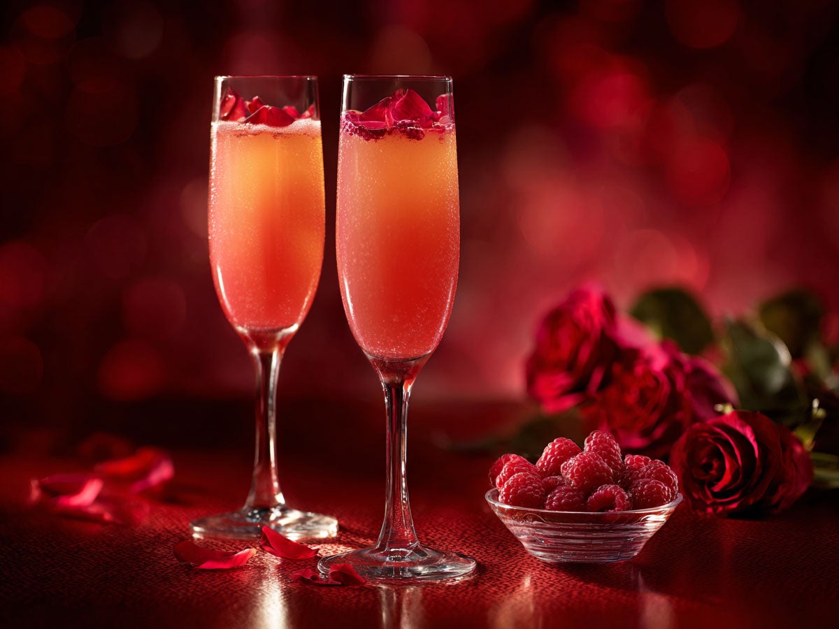 Two bright pink drinks served in champage glasses, next to the glass roses and raspberries are placed as decoration. Created by AI. Edited by Pernod Ricard Sweden