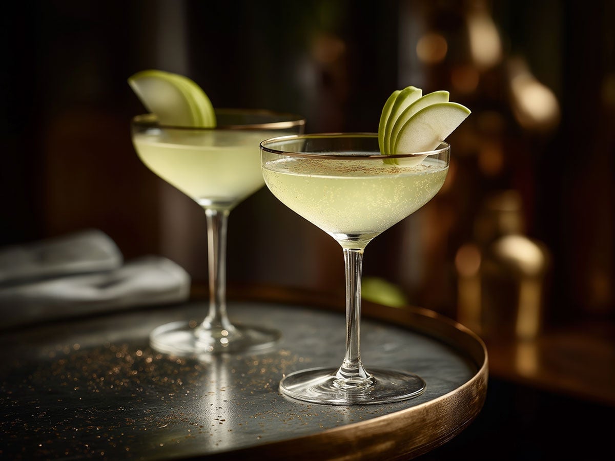En Appletini serveret i et coupeglas med en skive æble på kanten af glasset.